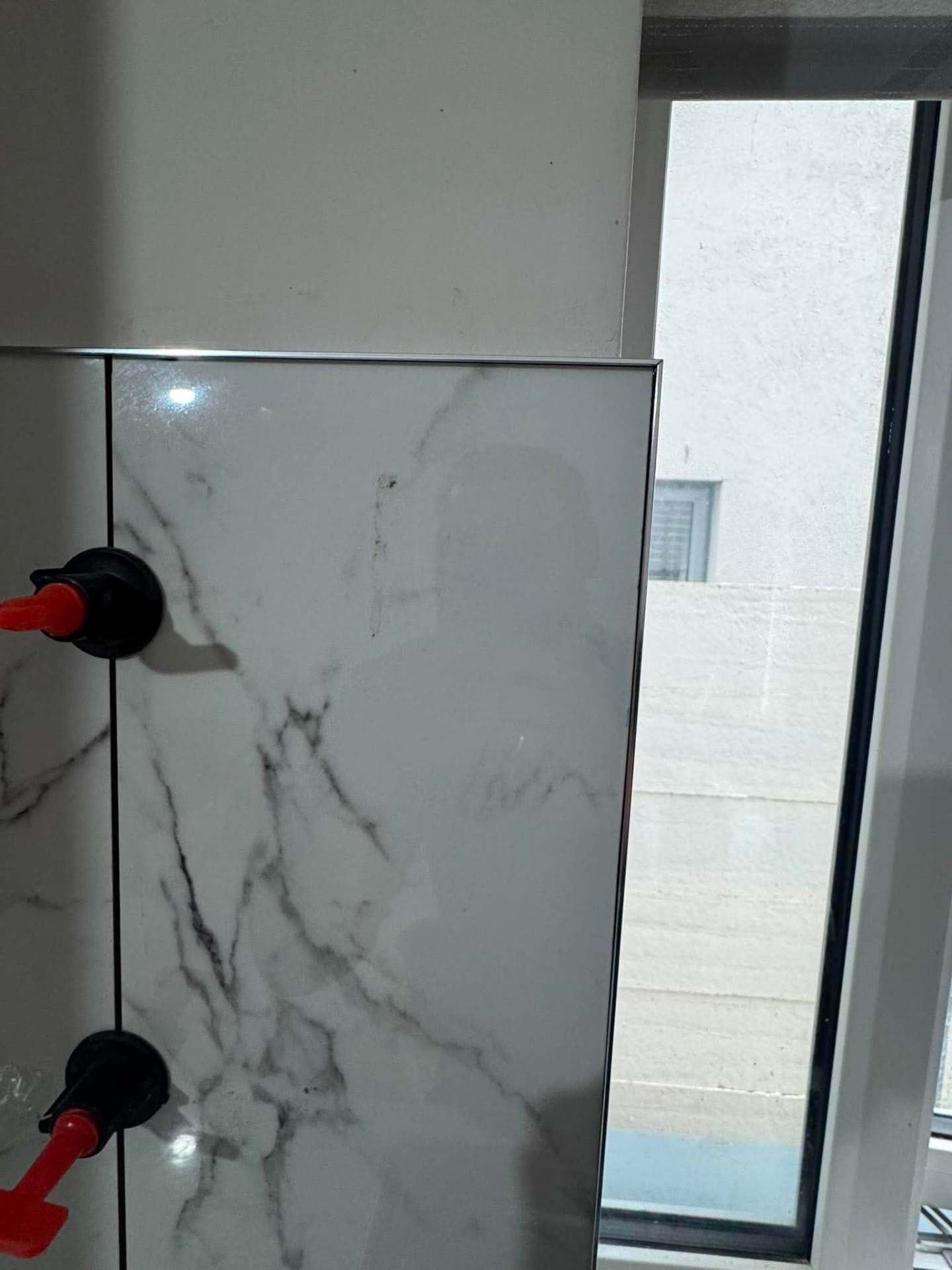 Large-format Calacatta porcelain kitchen splashback during install with red levelling clips